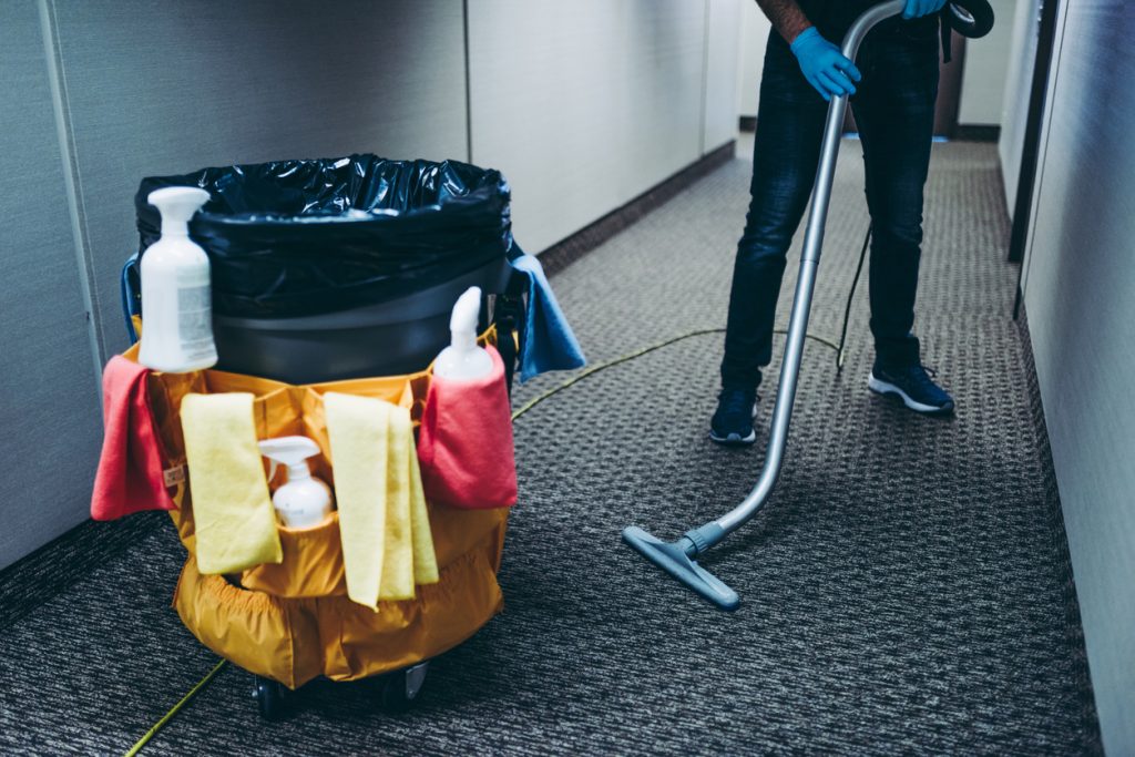 Janitor cleaning corridor of office with vacuum
